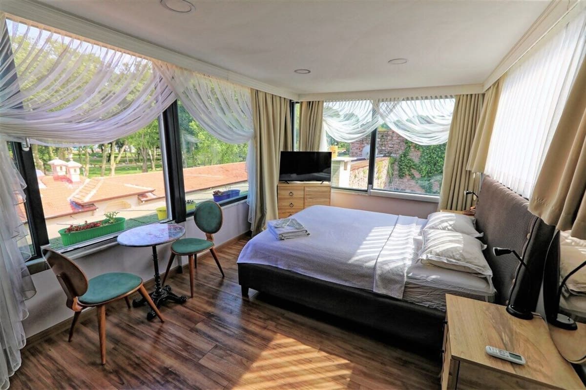 A hotel room with a bed, a TV, a desk with a chair, and a window with curtains.