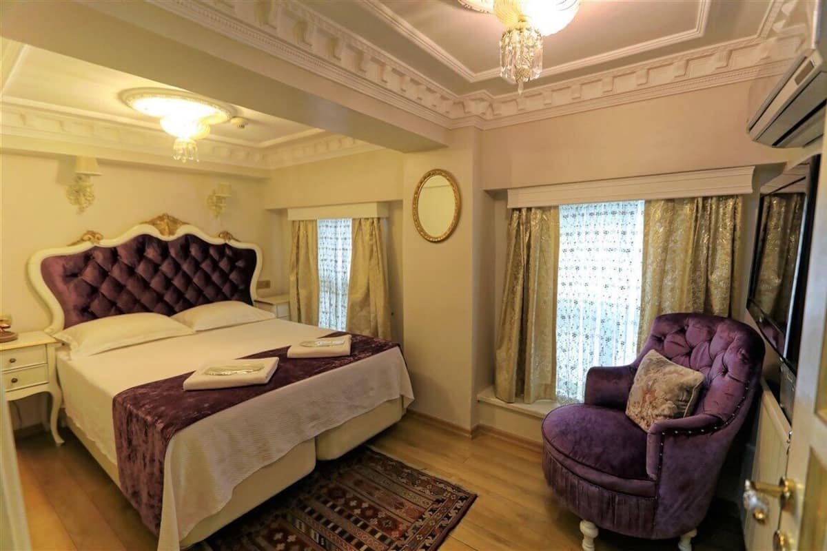 A bedroom with a large bed, a chair, a mirror, and a chandelier.