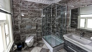 A modern bathroom with a glass-enclosed shower, a white sink, and marble walls. - Romantic Mansion (Istanbul)