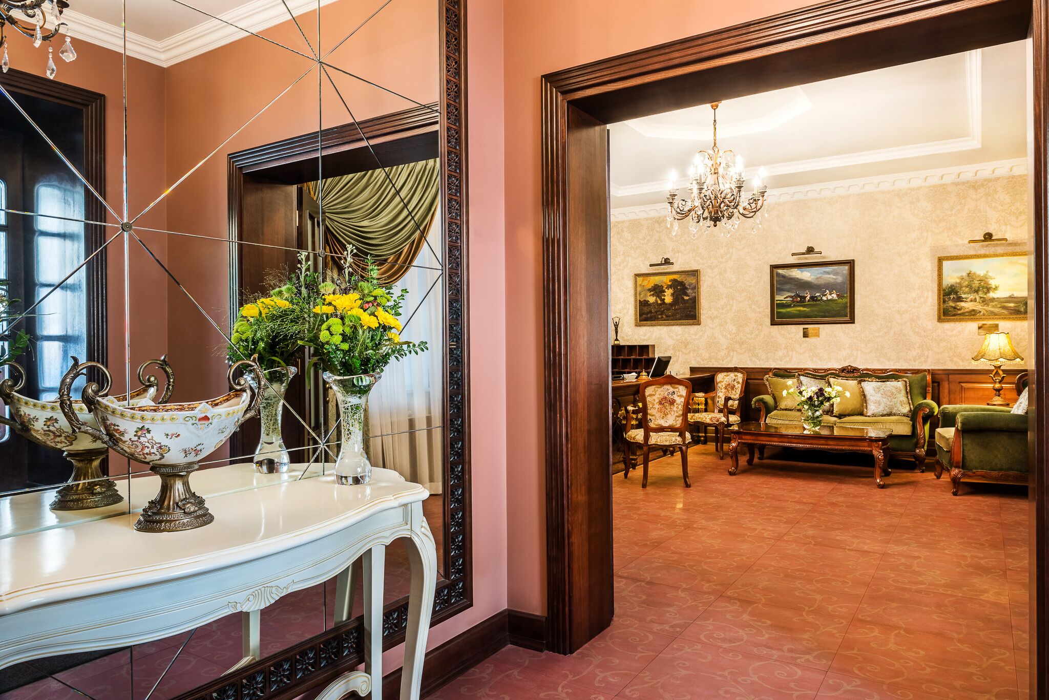 A room with a large mirror, a console table with decorative items, a sofa set, and a chandelier.