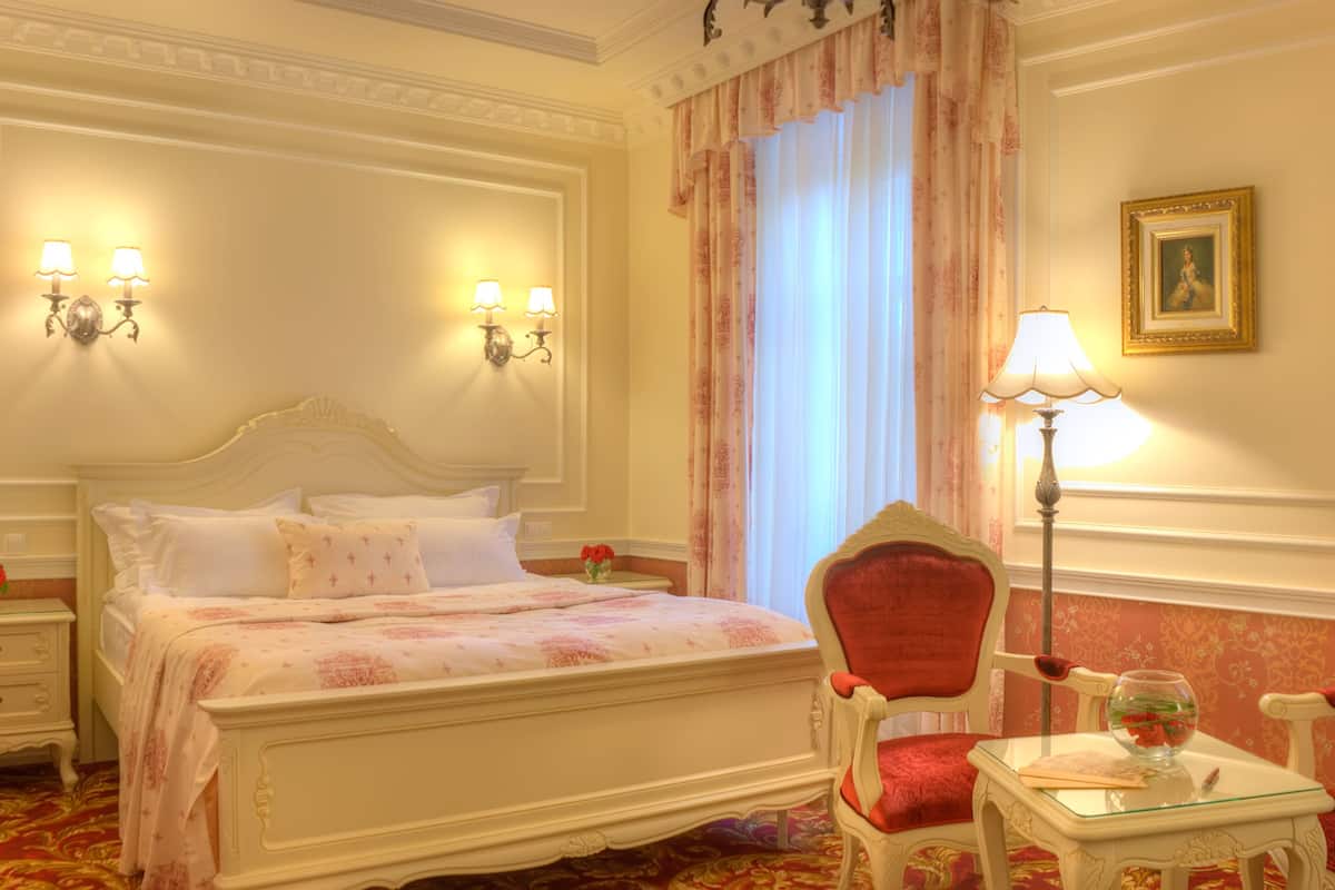 A hotel room with a bed, two chairs, a nightstand, a lamp, and a painting on the wall.
