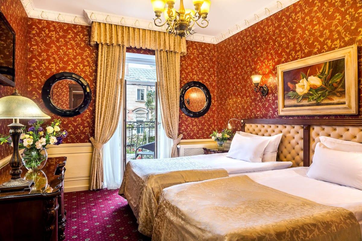 A hotel room with a large bed, a chandelier, a mirror, and a painting.