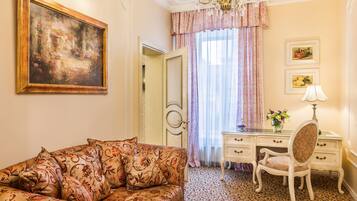 Una habitación con sofá, escritorio, silla, candelabro y un cuadro en la pared.