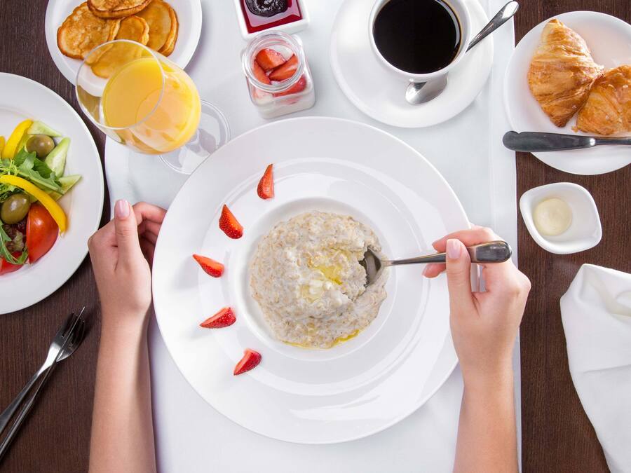 A breakfast setting with a plate of cereal, a glass of orange juice, croissants, and a cup of coffee.