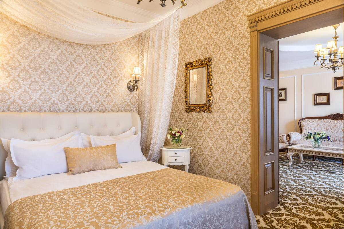 A luxurious bedroom with a large bed, a nightstand with a vase of flowers, and a mirror on the wall.