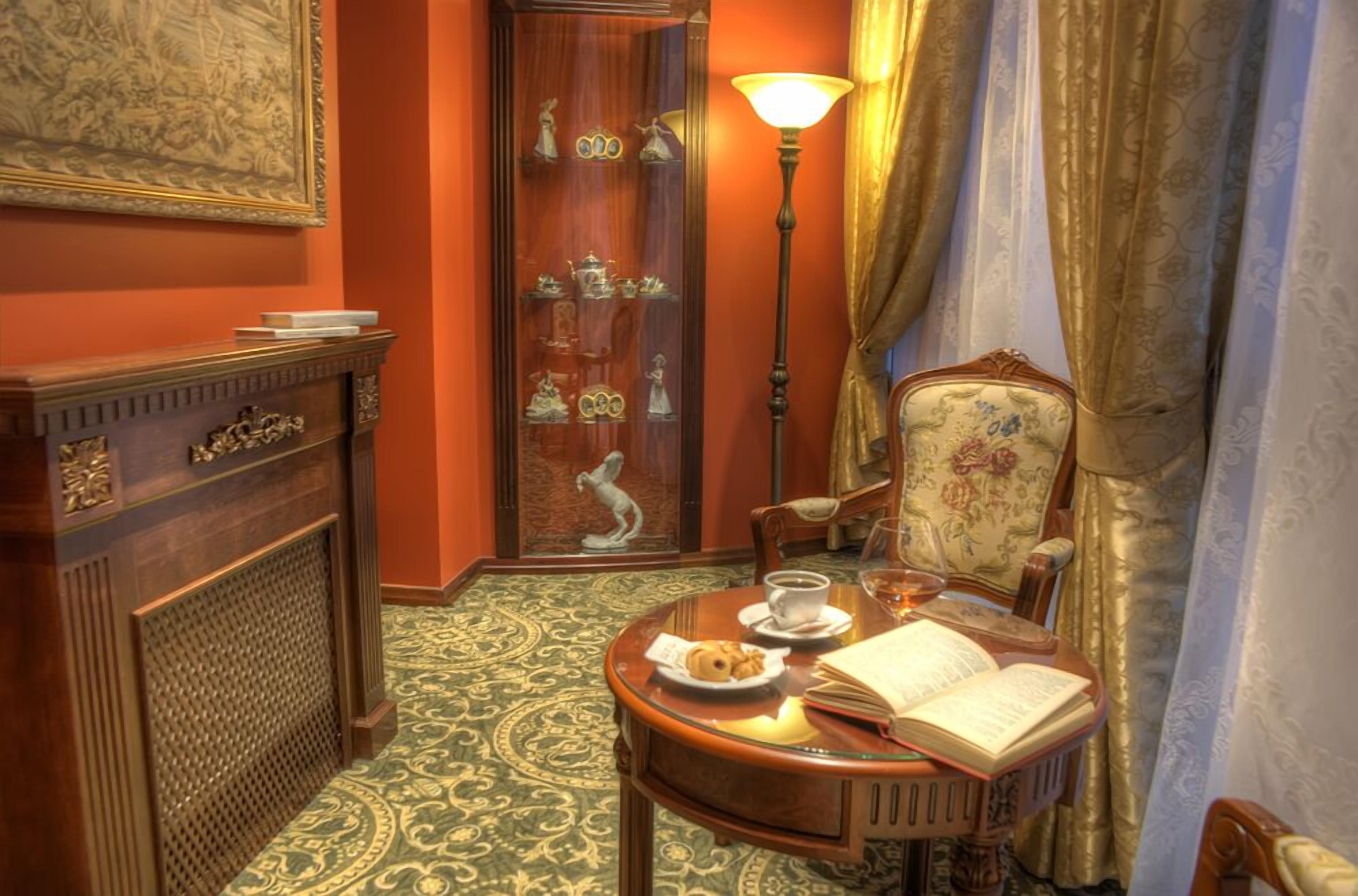 Una habitación con un armario de madera, una mesa con un libro y un plato de comida, una lámpara y una silla con tapicería floral.