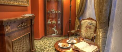 Una habitación con un armario de madera, una mesa con un libro y un plato de comida, una lámpara y una silla con tapicería floral.