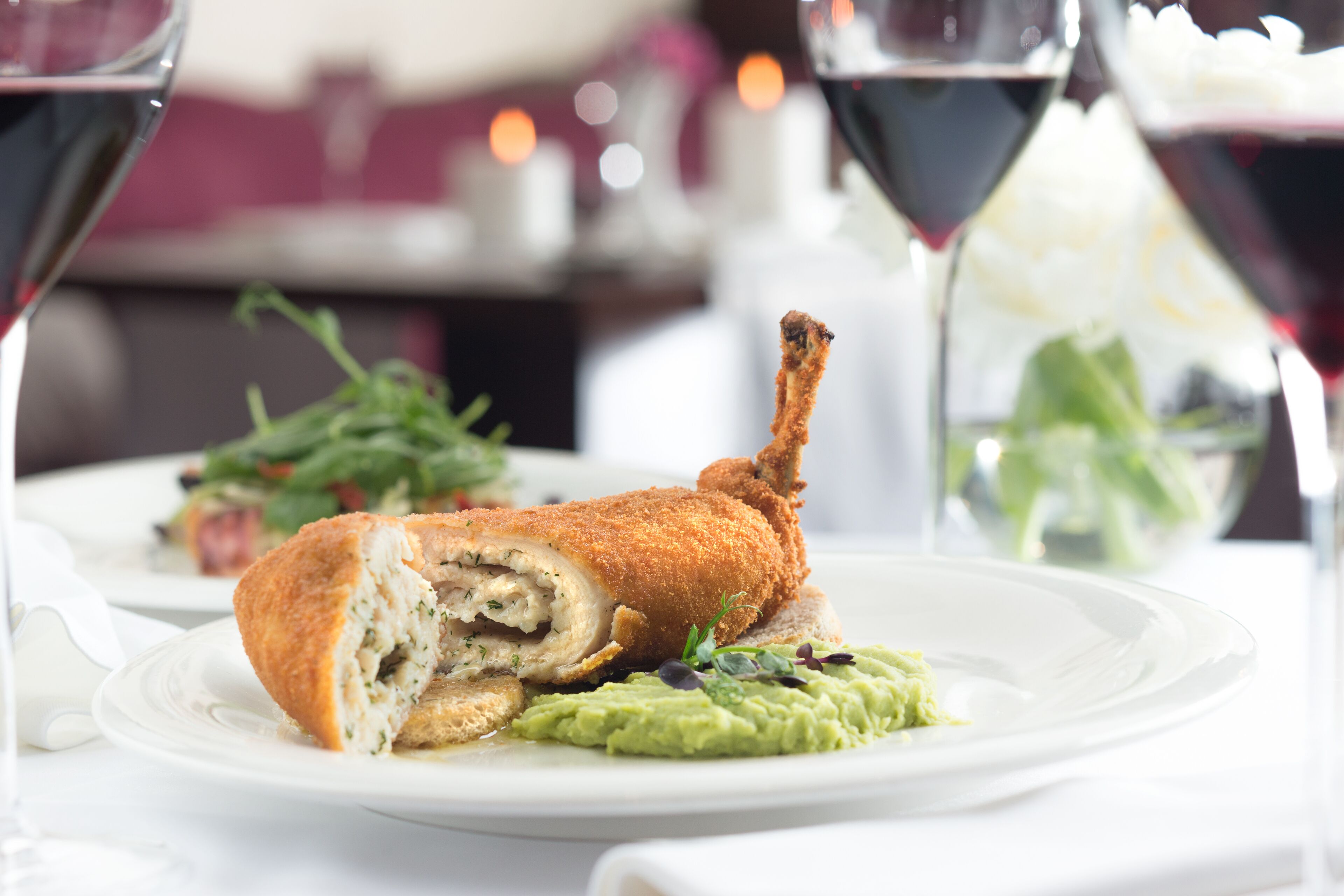 A plated dish with breaded chicken, avocado, and greens, accompanied by wine glasses.
