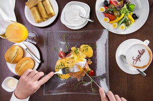 Un desayuno con huevos Benedict, un vaso de jugo de naranja y una taza de café con el nombre 'Sophie'.