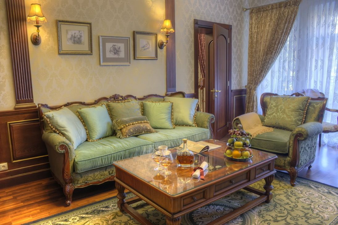 Una habitación tradicional con un sofá verde, un sillón a juego, una mesa de centro de madera con un centro de frutas y lámparas de pared.