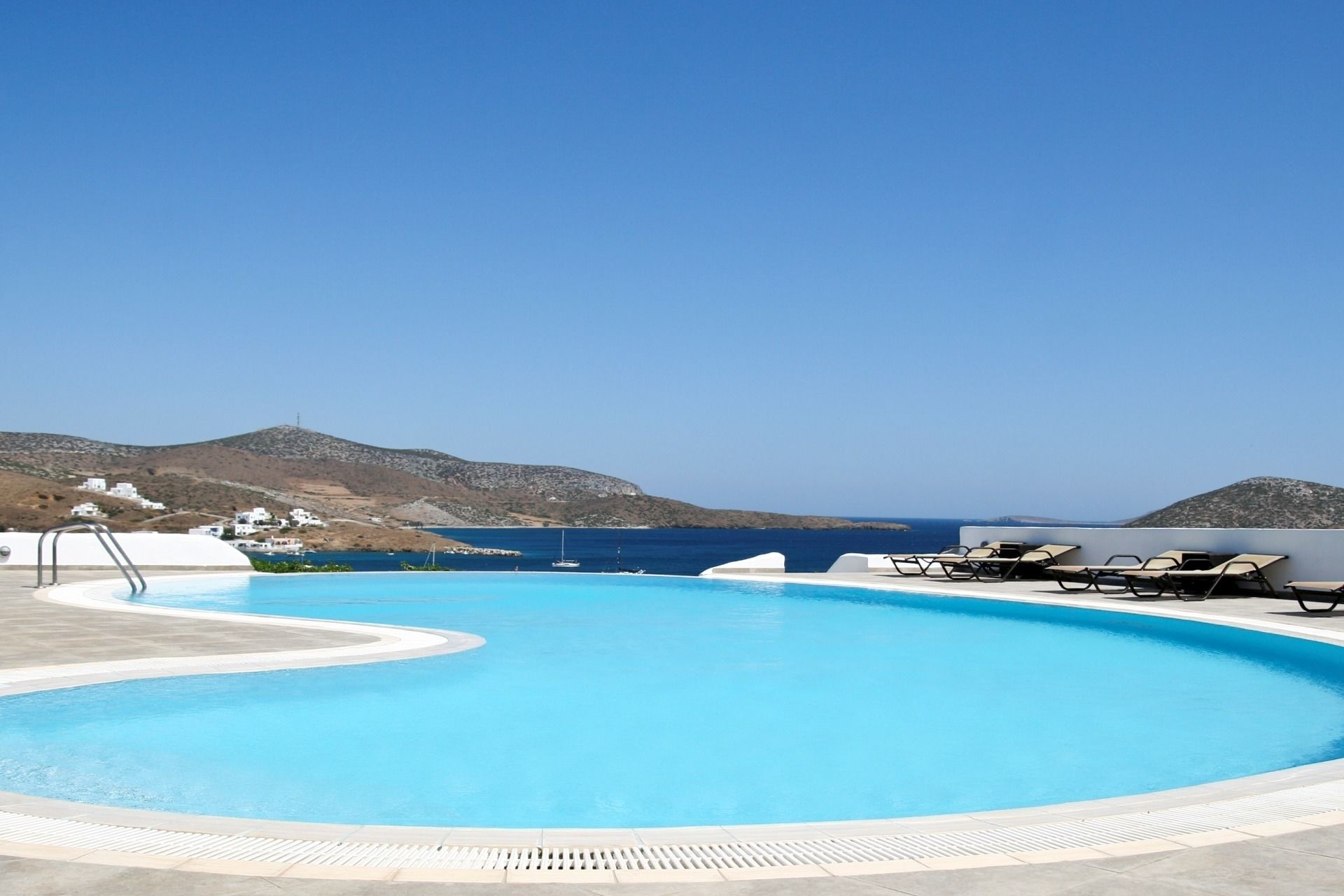 Une piscine d’un bleu éclatant, dotée de chaises longues et offrant une vue sur la mer et les collines.