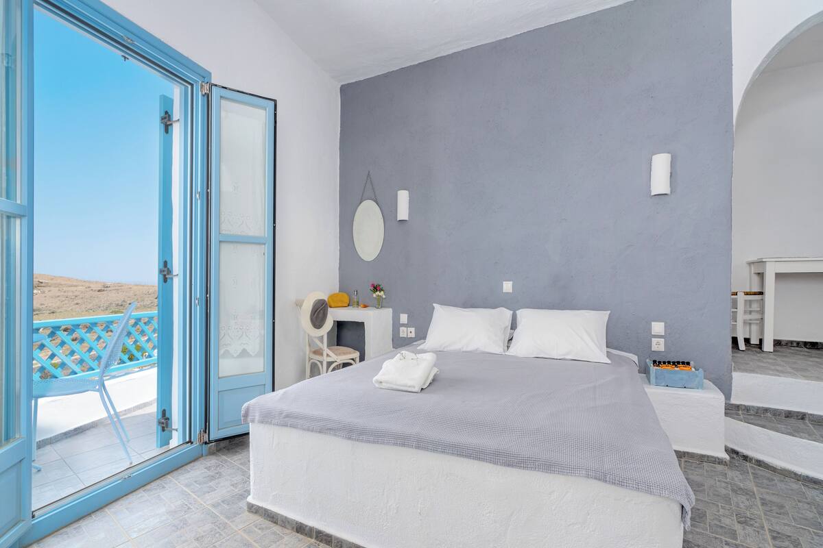 Ein Schlafzimmer mit Bett, Schreibtisch und Stuhl. Durch eine offene Tür ist der Strandblick zu sehen.
