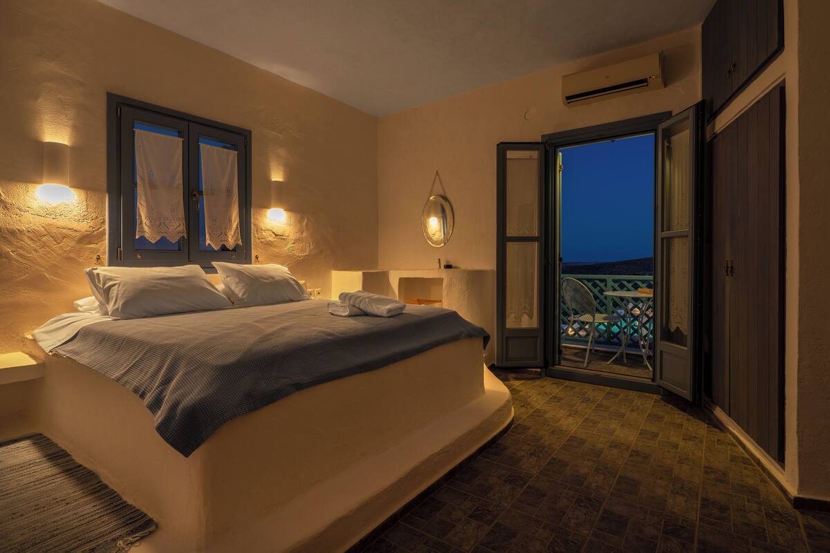 Ein Schlafzimmer mit einem Bett, einem Nachttisch, einer Wandlampe und Blick auf den Balkon.
