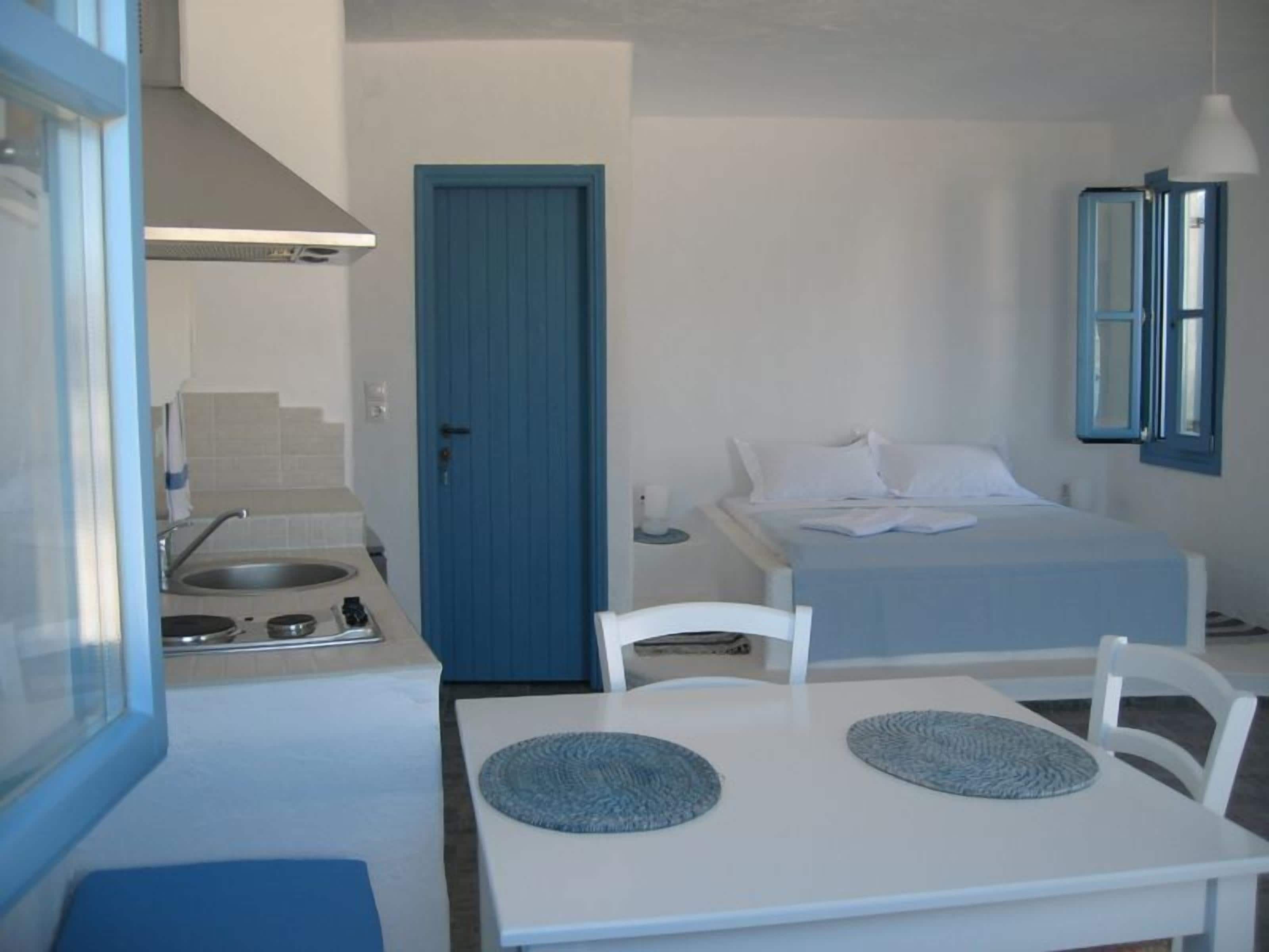 A compact hotel room with a kitchenette, a bed with white bedding, a small bedside table, and a mirror.