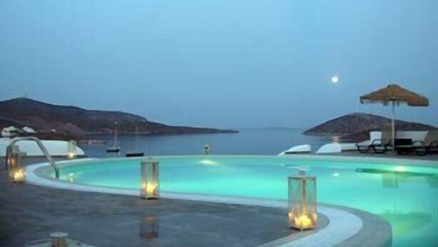 A pool area with a view of the sea and hills, surrounded by lounge chairs and umbrellas. - Castellano Village (Astypalaia)