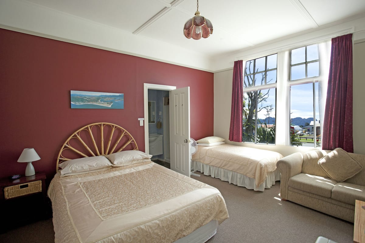 A bedroom with a large bed, two bedside tables, a chair, and a window with curtains.