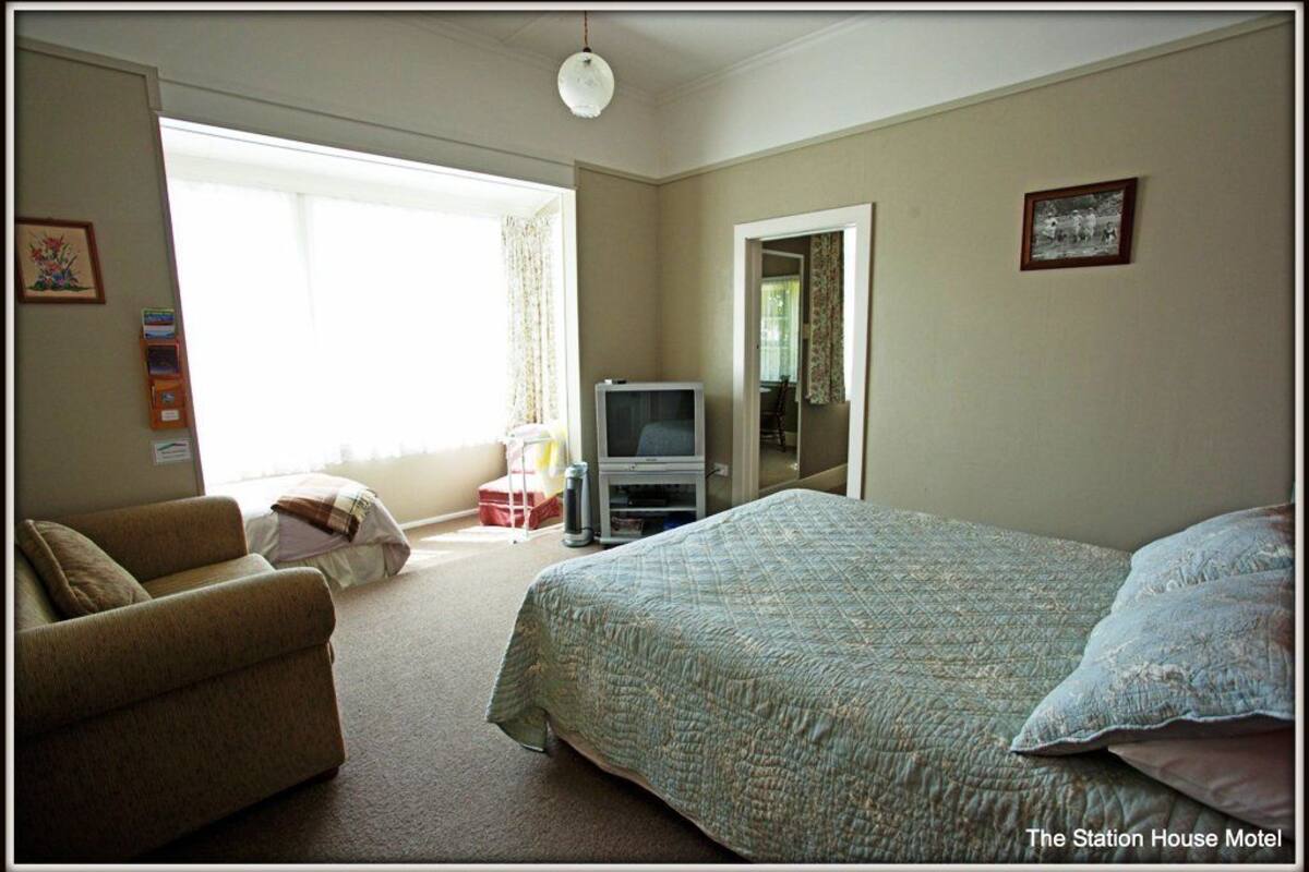 A bedroom with a bed, a sofa, a television, and a window with curtains.