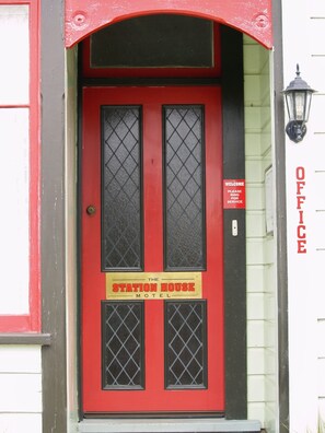Eine rote Tür mit einem Schild, auf dem „The Station House Motel“ steht, und einem „Willkommen“-Schild darüber.