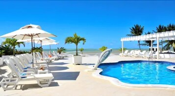 Una piscina al aire libre, sombrillas, sillones reclinables de piscina