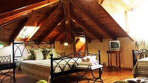 A bedroom with a sloped ceiling, a bed with a metal frame, a bedside table, a chair, and a television on a stand. - Pension Filyra (Nafplio)