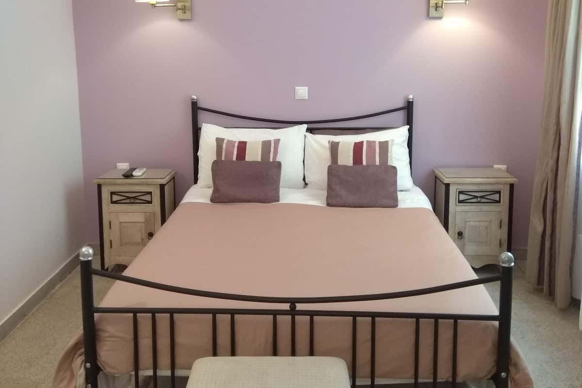 Una cama individual con cabecera, dos mesitas de noche, un banco y dos lámparas de pared.