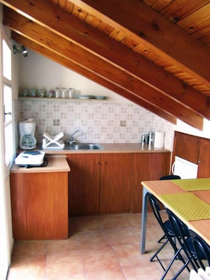 Una pequeña cocina con armarios de madera, salpicadero de azulejos, un lavamanos y una encimera con cafetera y báscula.