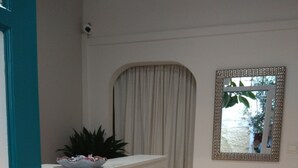 A reception desk with a sign reading "Pension Filya," a grey upholstered chair, a decorative mirror, and a curtain. - Pension Filyra (Nafplio)