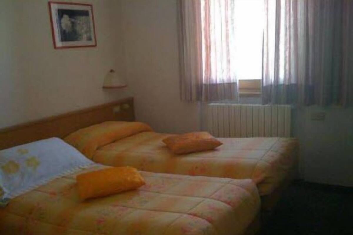 Una habitación de hotel con dos camas, una mesita de noche, una lámpara y una ventana con cortinas.