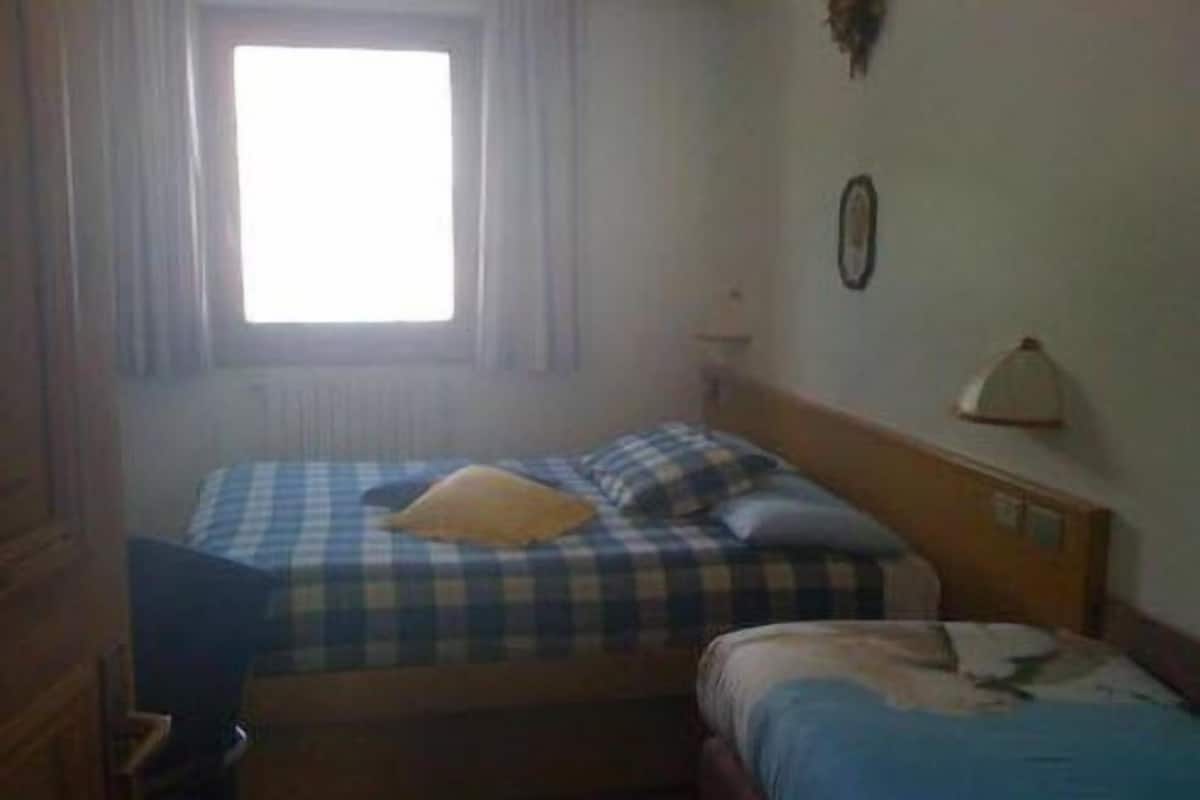 Una habitación con dos camas, una ventana con cortinas, un reloj de pared y una mesita pequeña.