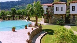 A pool area with a stone wall, palm trees, and a mountain backdrop.