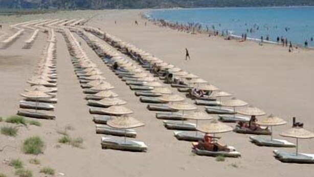 A beach with rows of umbrellas and lounge chairs, a sandy shore, and a clear view of the sea.