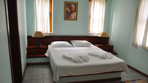 A neatly made double bed with white linens, two bedside lamps, a wooden headboard, and a patterned rug on the floor.