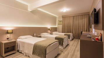 A hotel room with three beds, a desk, a TV, and a minibar.