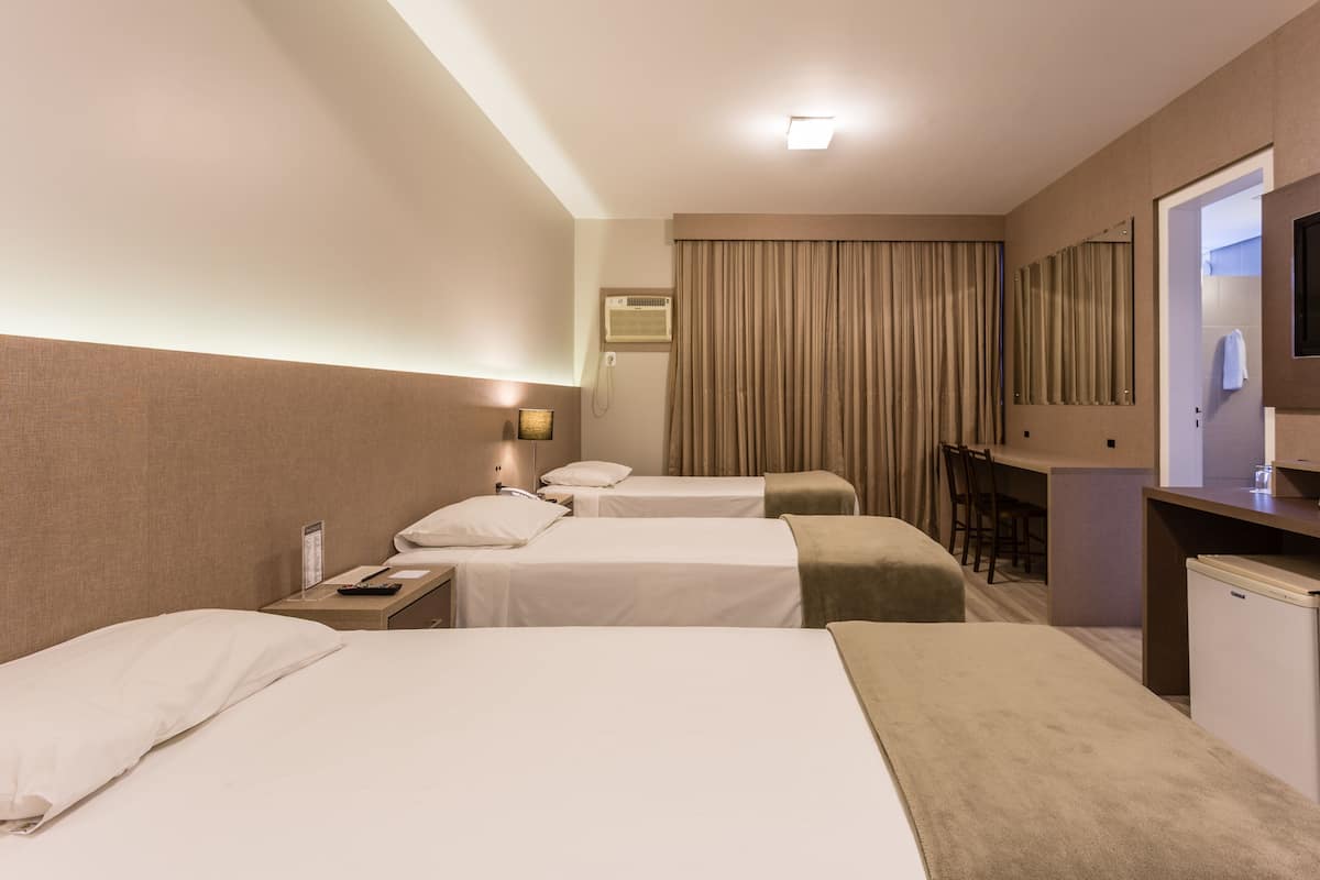 A hotel room with two beds, a desk, a chair, a small refrigerator, and a mirror.