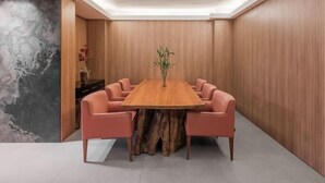 Una sala conferenze con un lungo tavolo di legno circondato da sei sedie, un vaso con fiori e un grande quadro astratto sulla parete sinistra.