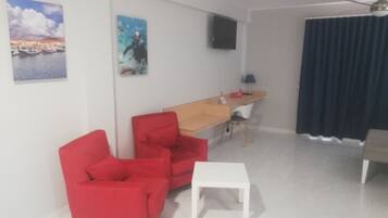 A modern living room with a wooden desk, two red chairs, a white table, and a ceiling fan.