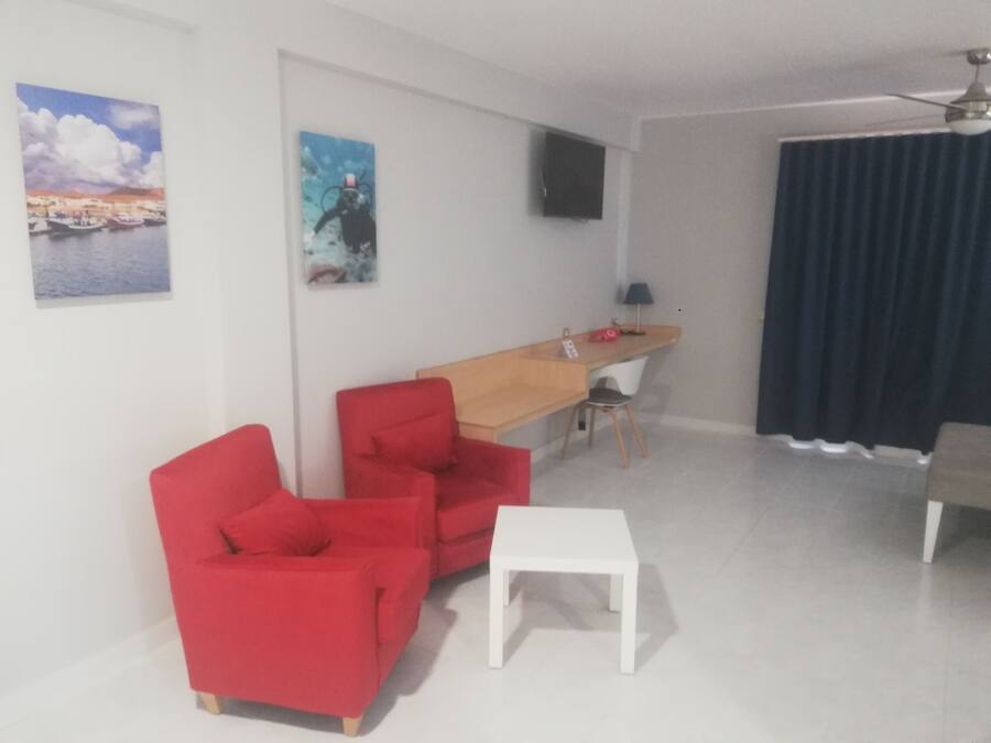 A modern living room with a wooden desk, two red chairs, a white table, and a ceiling fan.