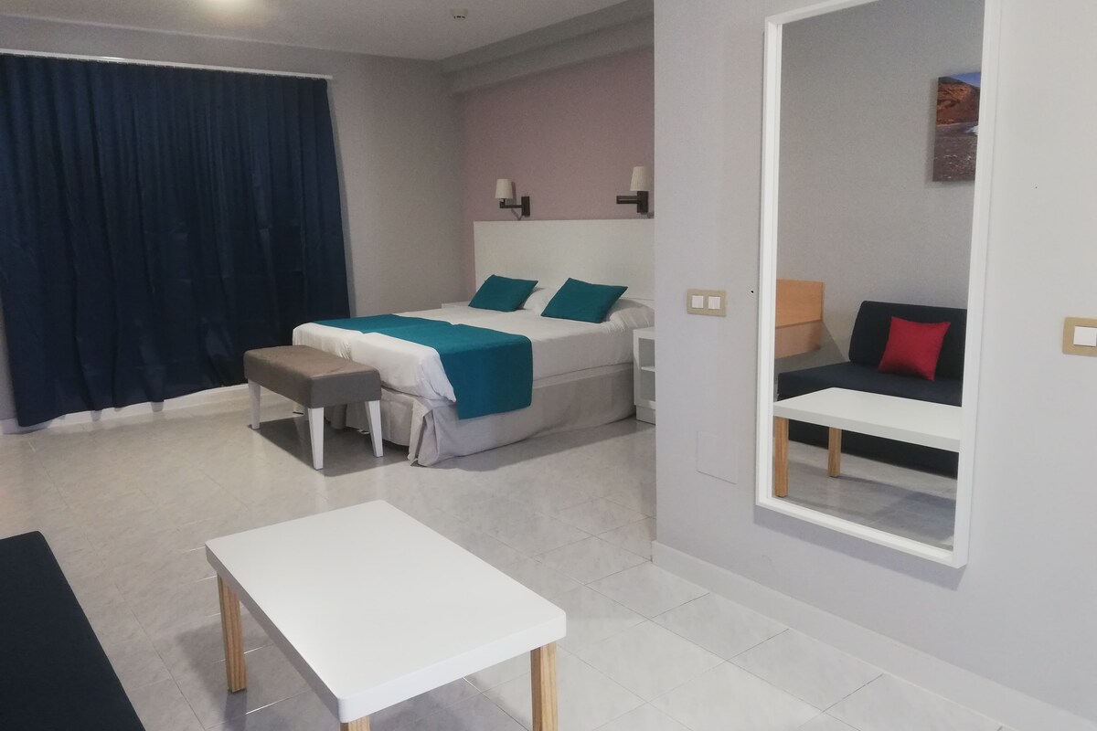 A modern hotel room with a bed, a bench, a table, and a mirror.