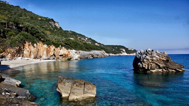 A coastal landscape with clear blue waters, rocky formations, and a hilly backdrop. - Aleka's House (Zagora-Mouresi)