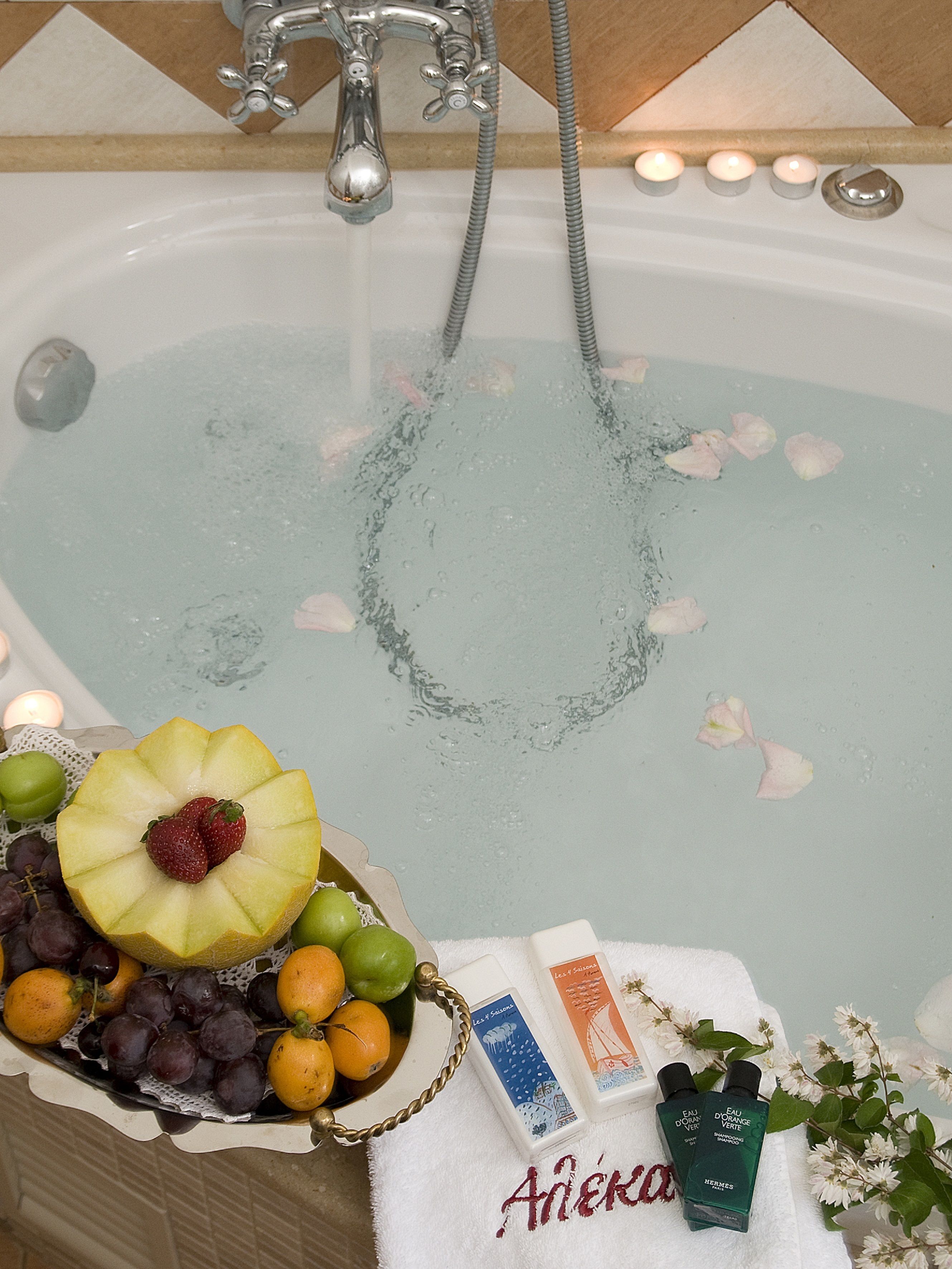 Una bañera llena de agua, un frutero con uvas, naranjas y una fresa, y dos botellas de champú.