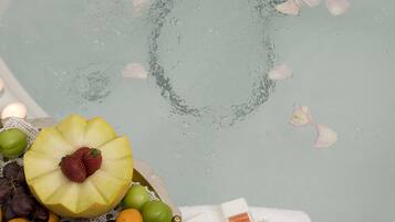 Una bañera llena de agua, un frutero con uvas, naranjas y una fresa, y dos botellas de champú.