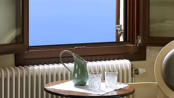 Ein Zimmer mit Fenster, Heizkörper, Tisch mit Krug und Gläsern sowie einem Stuhl.