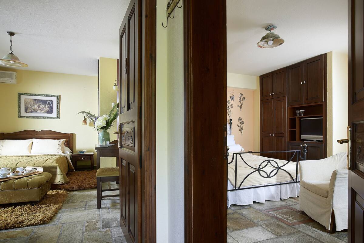 Un dormitorio con cama, mesita de noche y tocador. Hay un baño con inodoro, lavabo y espejo. La habitación tiene una puerta de madera y una ventana.