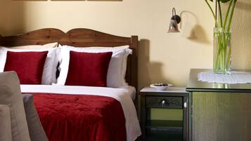 Una cama bien hecha con ropa de cama roja y blanca, una mesita de noche con un jarrón de flores y una pared con cuadros abstractos.