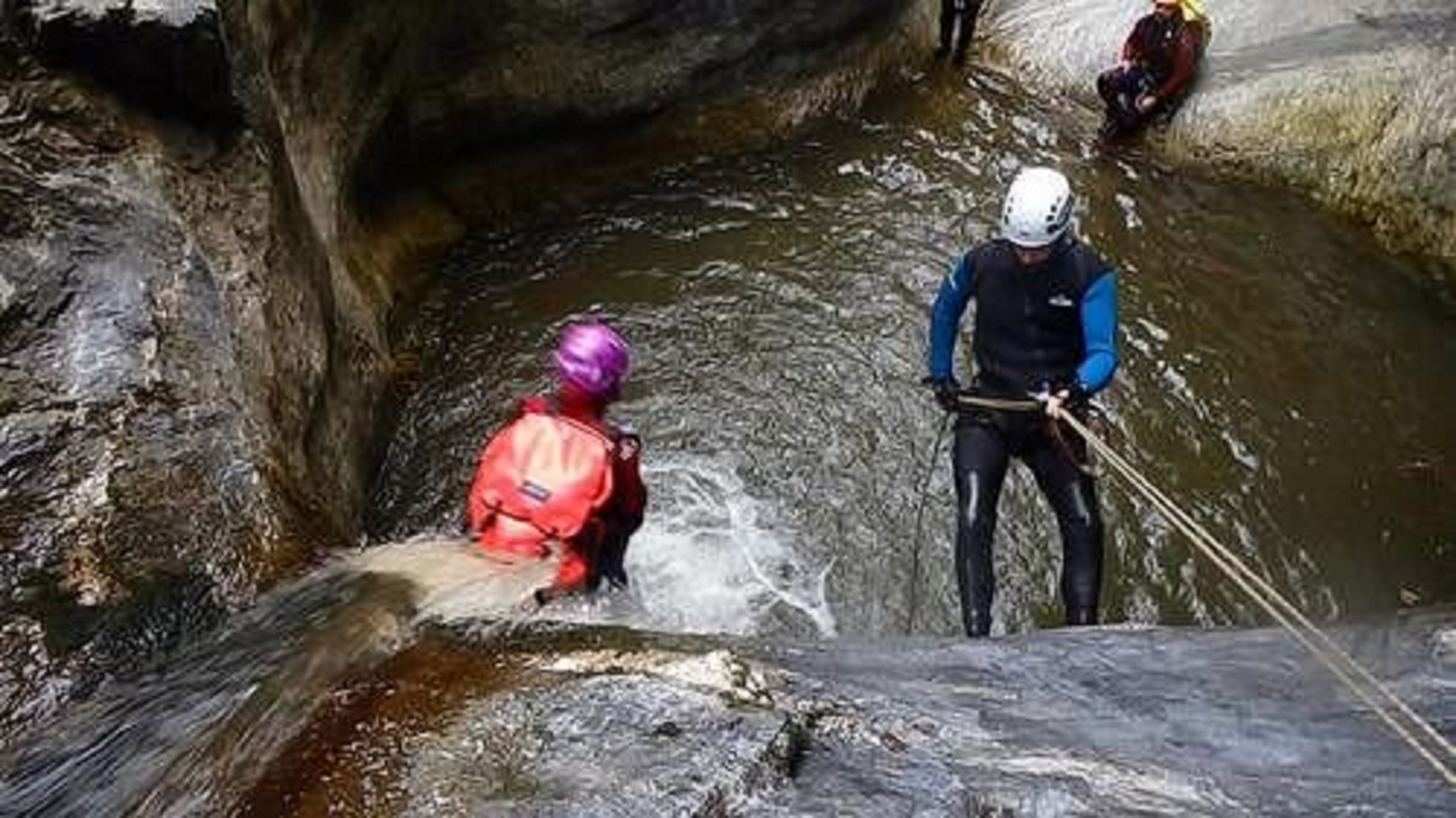 Un estrecho canal acuático con dos personas en botas de agua, una vestida de rojo y la otra de azul, recorriéndolo.