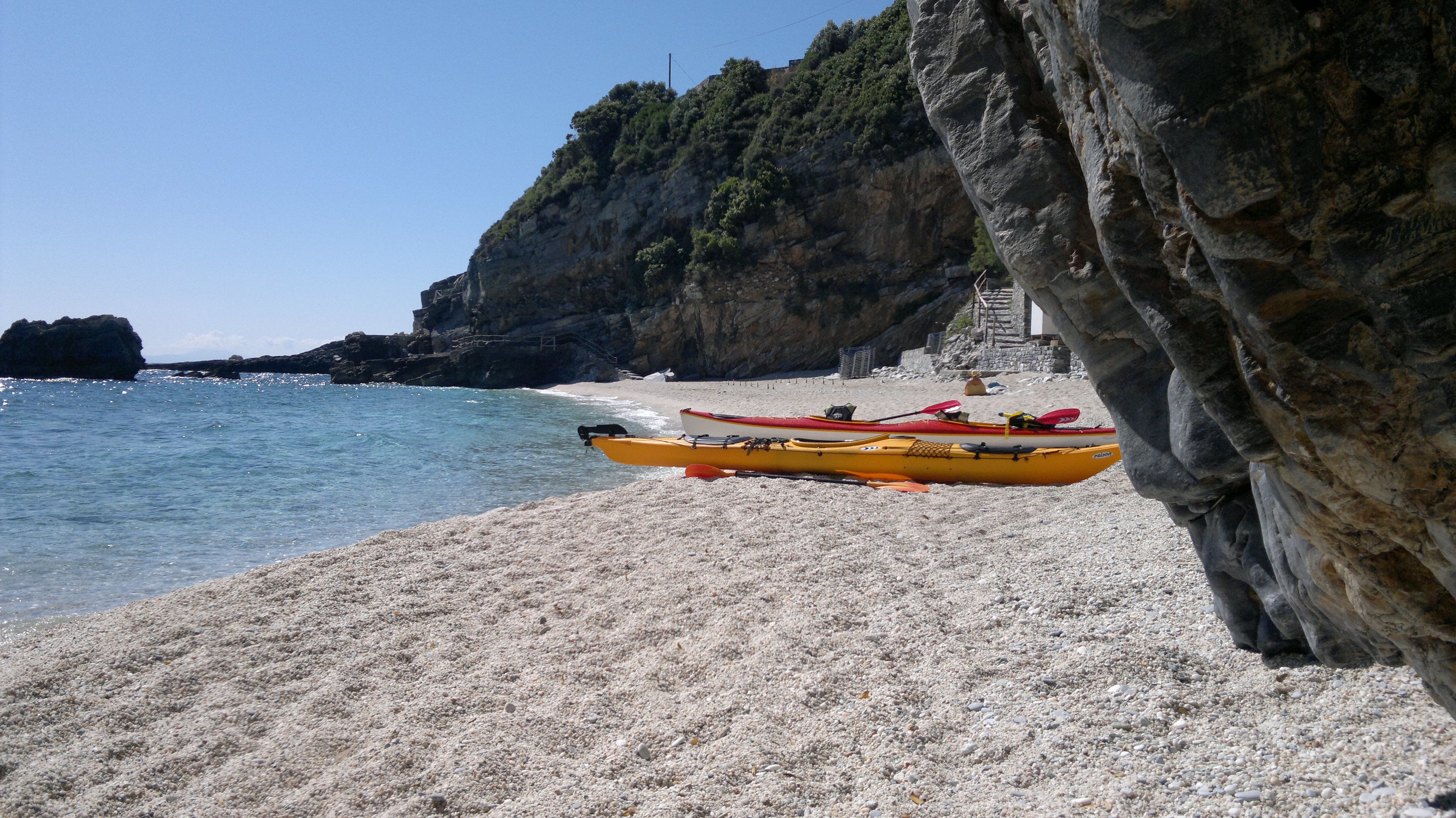 A beach with kayaks and a staircase leading up a rocky cliff.