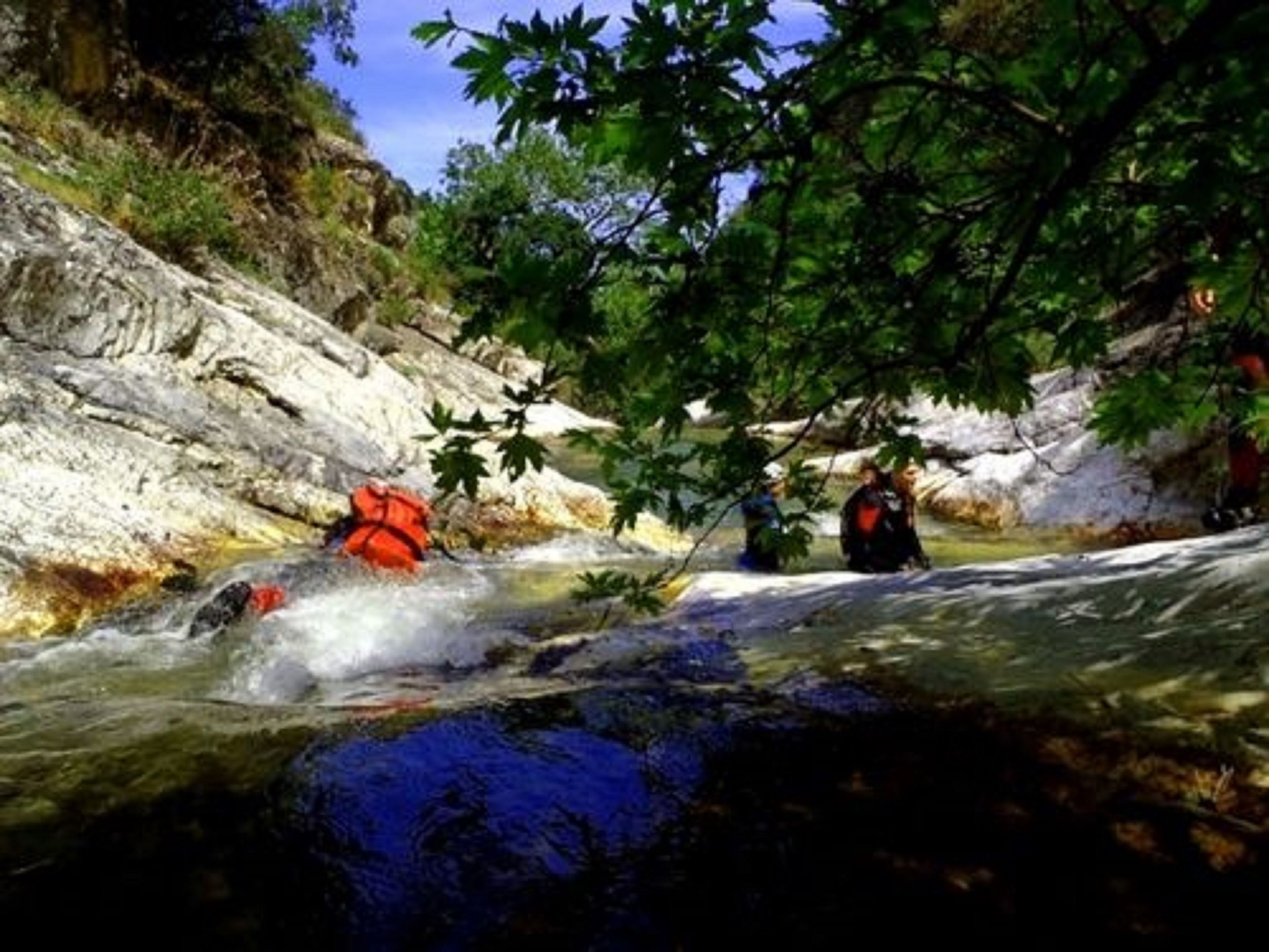 Un fiume con una riva rocciosa e persone che fanno il bagno.