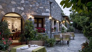 A stone building with a patio area featuring tables and chairs, surrounded by potted plants and flowers. - Aleka's House (Zagora-Mouresi)