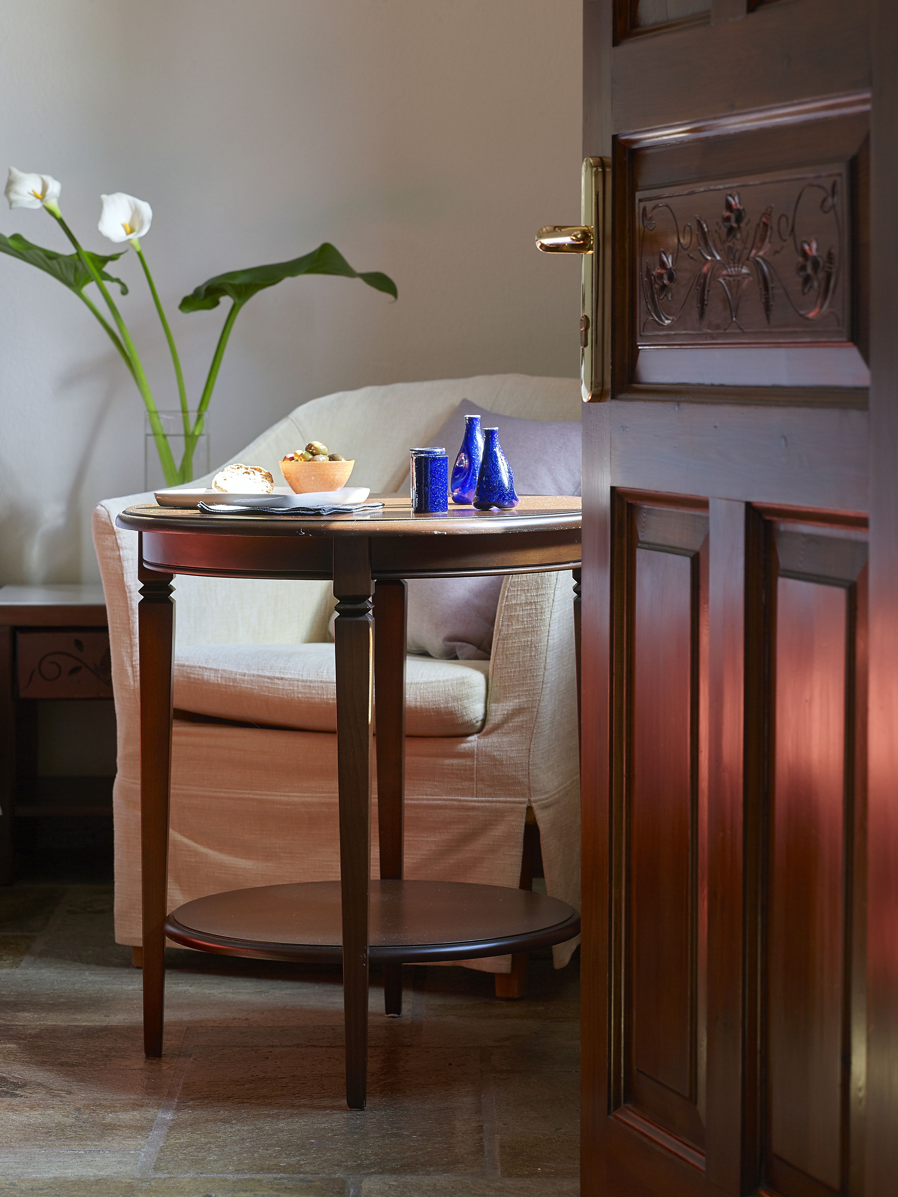 Uma mesa de madeira com uma tigela e vasos azuis, uma cadeira e uma porta com um painel decorativo.