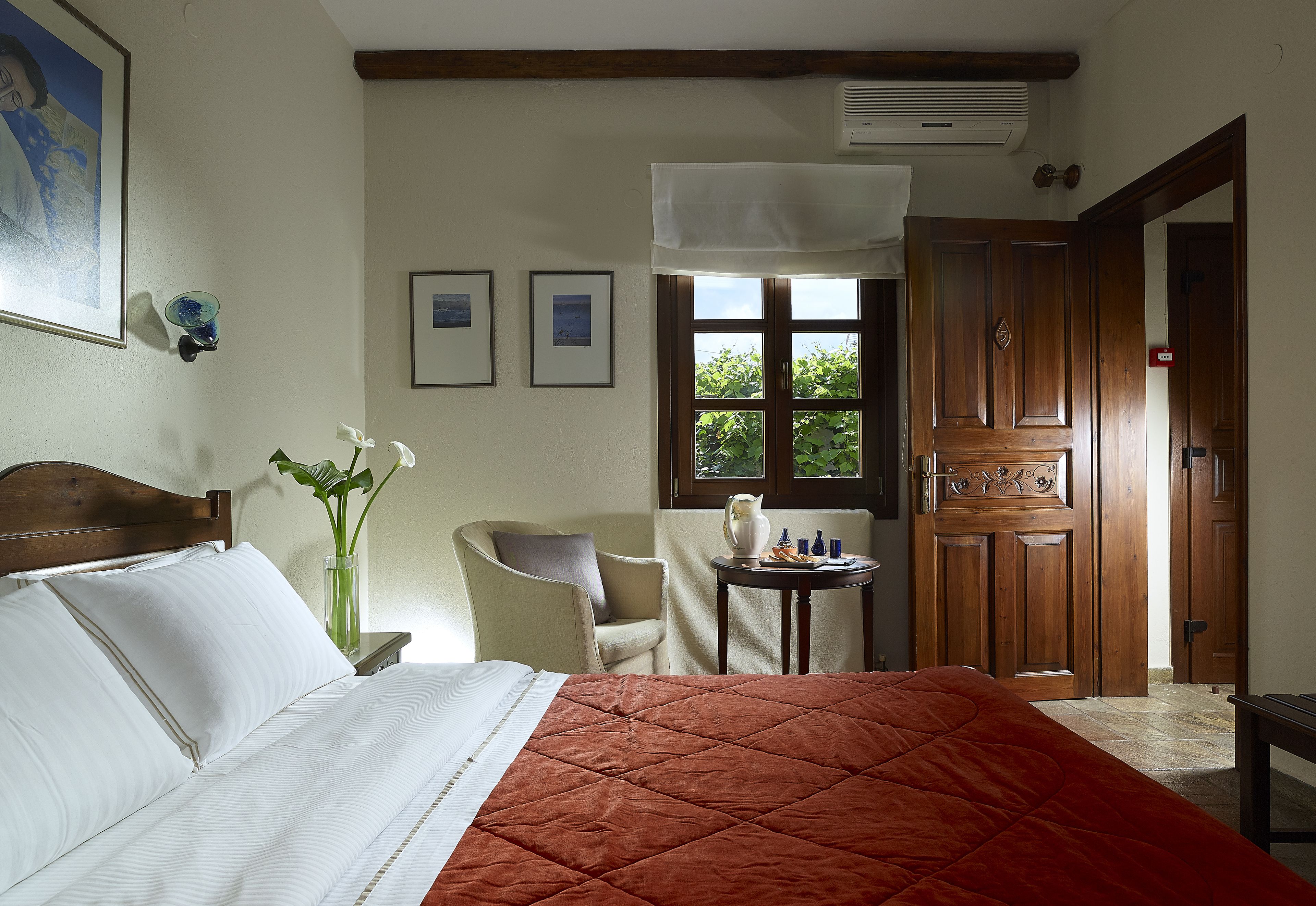 A hotel room with a bed, a chair, a small table, and a door.